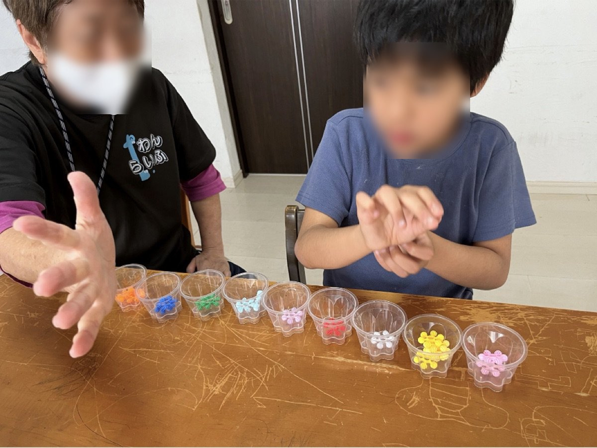 支援員と子どもが、色分けしたビーズを並べて取り組んでいる様子