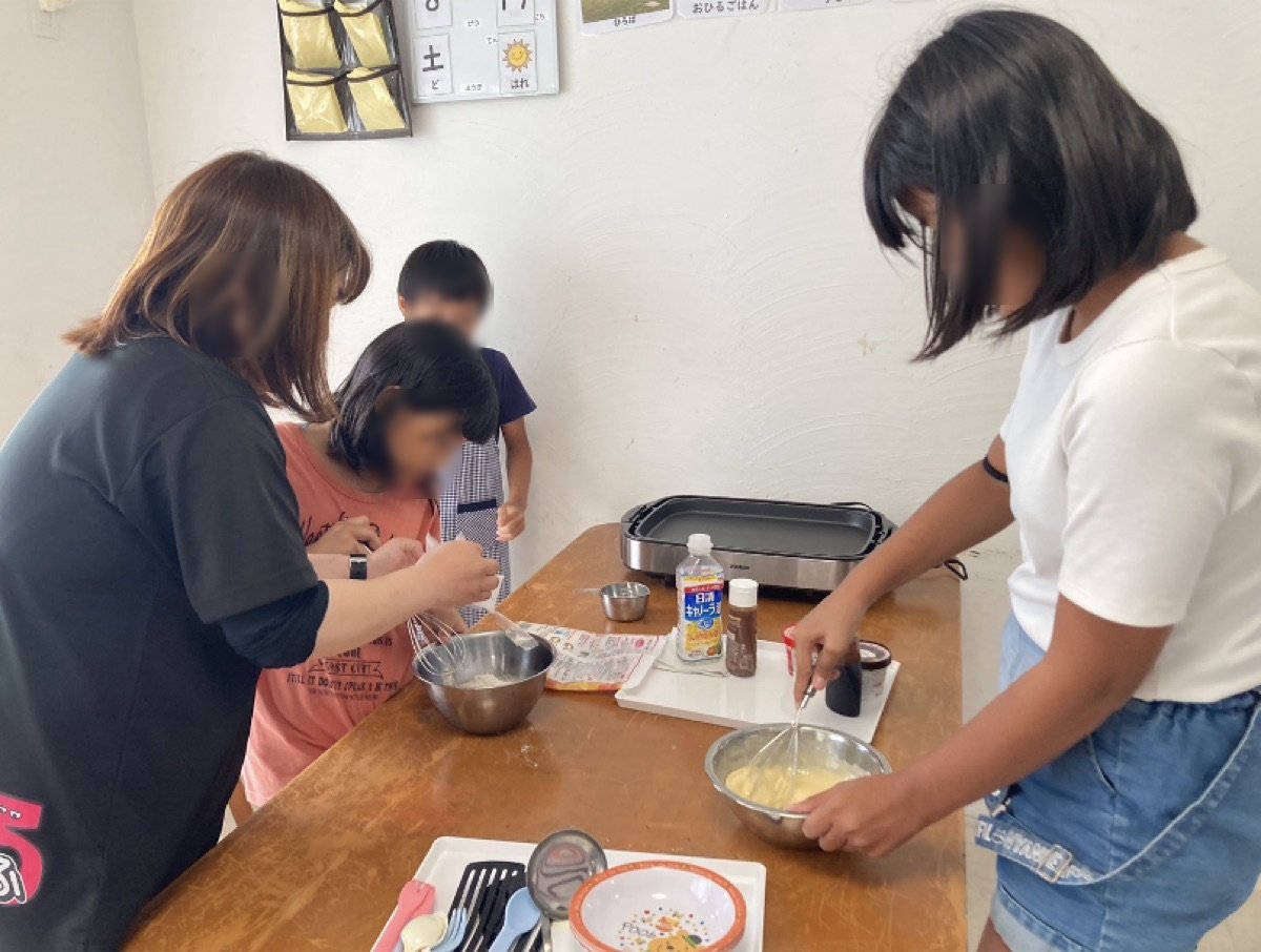 調理台を囲んで、支援員と子どもたちが一緒におやつを作っている様子